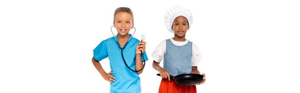 concepto panorámico de niños multiculturales en trajes de diferentes profesiones que sostienen sartén y estetoscopio aislados en blanco  - Foto, Imagen