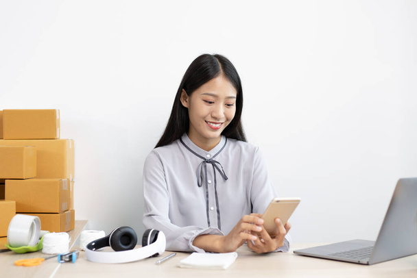 Nuoret aasialaiset naiset myyvät tuotteita verkossa ja käyttävät matkapuhelimia keskustelemaan asiakkaiden kanssa tilausten vahvistamiseksi, tuotteiden myymiseksi verkossa tai freelance-työn tekemiseksi kotona. - Valokuva, kuva