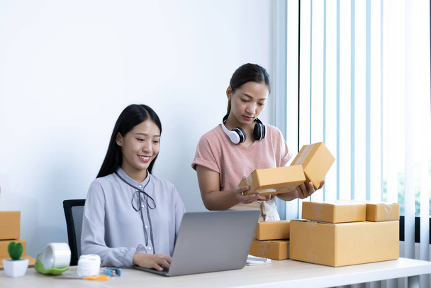 Dvě mladé asijské ženy chatovat s jasnými úsměvy na zákazníky, kteří nakupují on-line prostřednictvím notebooku a potvrdit objednávku uzavřít dohodu, Prodej produktů on-line nebo dělat práci na volné noze doma koncept. - Fotografie, Obrázek