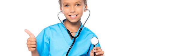 panoramic shot of kid in costume of doctor holding stethoscope while showing thumb up isolated on white  - Fotografie, Obrázek
