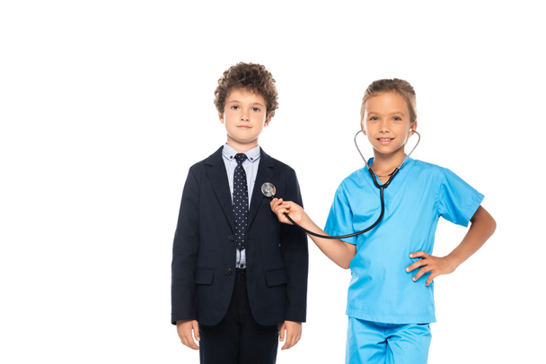 child in costume of doctor examining curly kid in formal wear isolated on white  - Foto, afbeelding