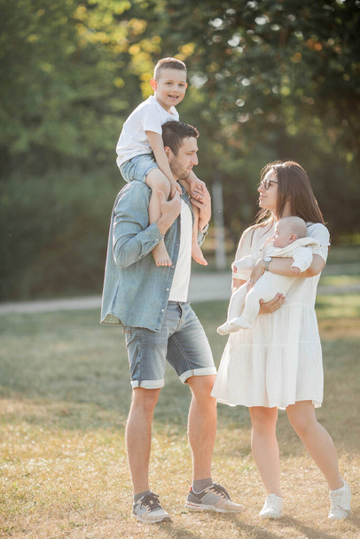 Young beautiful family walks in the park. Family portrait in the sunset light. Summer picnic. Spring. - 写真・画像