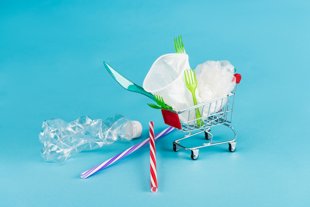 disposable plastic objects in small shopping cart on blue background - Fotografie, Obrázek