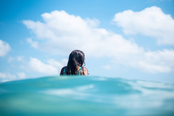 Portrait of surfer girl on white surf board in blue ocean pictured from the water in Bali - Foto, Imagen