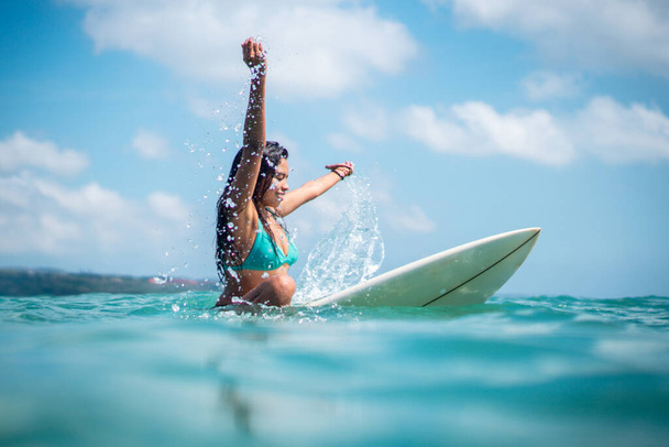 Portrait of surfer girl on white surf board in blue ocean pictured from the water in Bali - Photo, image
