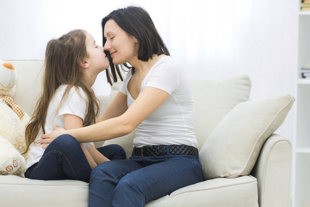 Young woman kissing little girl while sitting in bedroom. - Foto, Bild