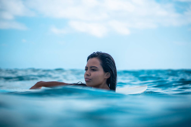 Portrait of surfer girl on white surf board in blue ocean pictured from the water in Bali - Foto, afbeelding