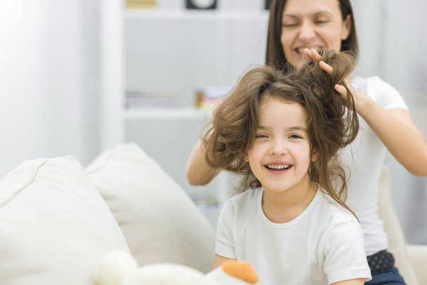 Photo of small girl with long dark messy hair and her mother brushing her hair. - Foto, immagini