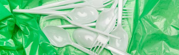 top view of white disposable cutlery on green plastic texture, panoramic shot - Photo, Image