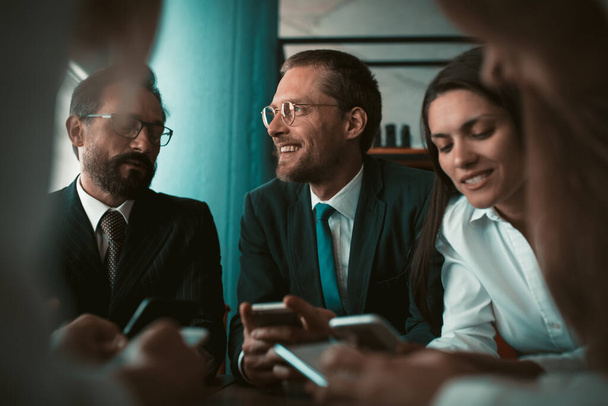 Group of smiling businesspeople using phones while communicating in meeting or negotiation. Business partnership concept. Tinted image - Fotografie, Obrázek