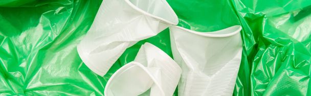 bovenaanzicht van witte verkreukelde wegwerpbekers op groene plastic textuur, panoramisch shot - Foto, afbeelding
