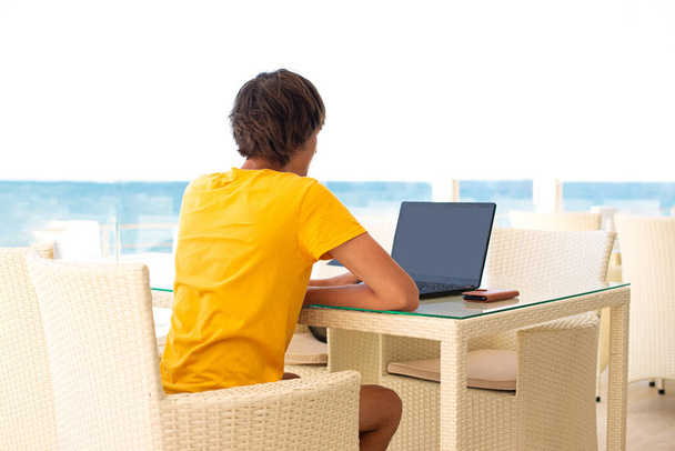 Lieu de travail dans un café avec vue sur la mer. Un homme travaillant sur un ordinateur portable dans un café. Copiez, maquillez-vous. les gens par derrière - Photo, image