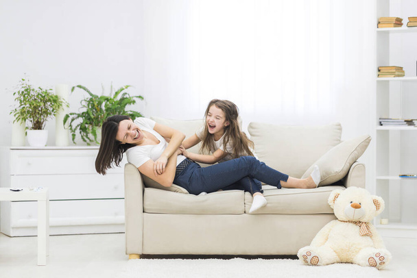 Photo of little girl playing with her mother on white sofa. - Фото, зображення