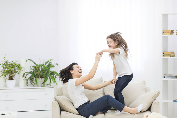 Smiling mother and daughter playing together in the living room. - Фото, зображення