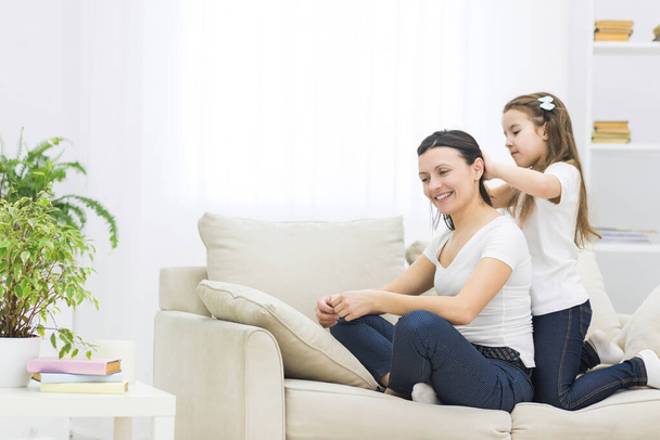 Photo of smiling mom with short dark hair and her beautiful little daughter who is brushing her hair. - Photo, Image
