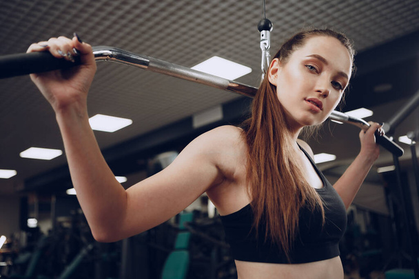 Atraktivní mladá žena dělá cvičení pro svaly paží a zpět v tělocvičně - Fotografie, Obrázek