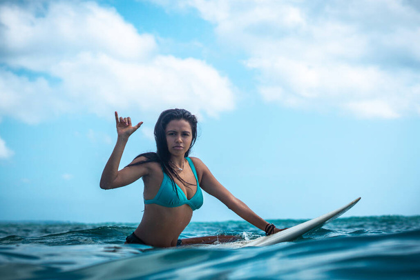 Portrait of surfer girl on white surf board in blue ocean pictured from the water in Bali - Photo, Image