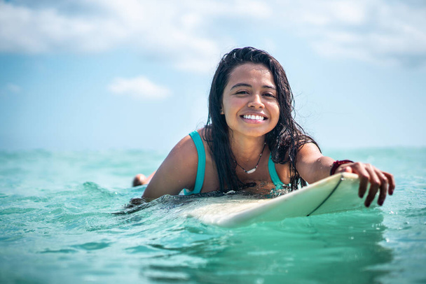 Portrait of surfer girl on white surf board in blue ocean pictured from the water in Bali - 写真・画像