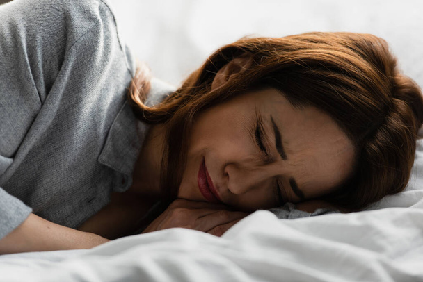 frustrovaná a brunetka žena se zavřenýma očima pláče na posteli - Fotografie, Obrázek