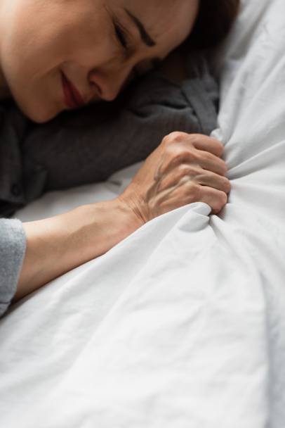 Ansicht von oben: Frustrierte und brünette Frau berührt Bettwäsche, während sie auf dem Bett weint  - Foto, Bild