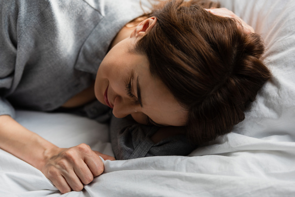 selective focus of frustrated and brunette woman touching bedding while crying on bed  - Foto, Bild
