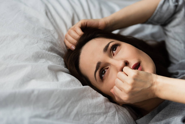 frustrado e morena mulher tocando rosto enquanto deitado na cama  - Foto, Imagem