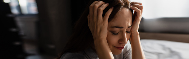 panoraama suunta järkyttynyt ja brunette nainen koskettaa hiukset itkiessään kotona - Valokuva, kuva