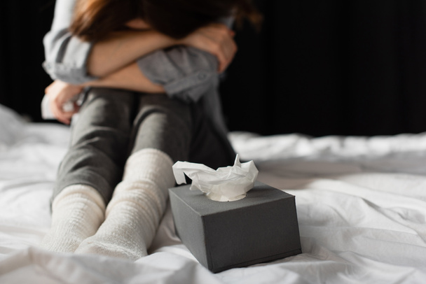 обрезанный вид на депрессивную женщину, сидящую на кровати рядом с коробкой ткани  - Фото, изображение