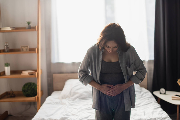 woman suffering from stomach ache in modern bedroom  - Фото, зображення
