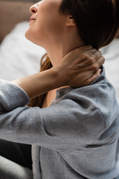 oříznutý pohled na brunetku ženy trpící bolestí krku v ložnici - Fotografie, Obrázek