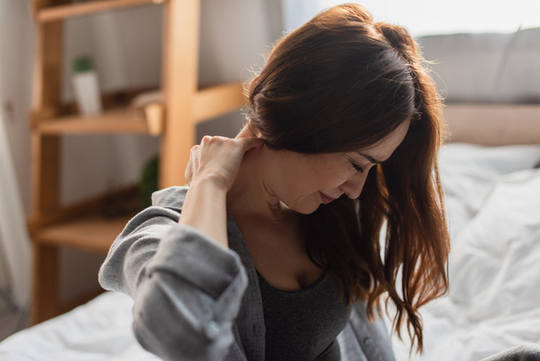 selective focus of upset brunette woman suffering from neck pain in bedroom - Fotoğraf, Görsel
