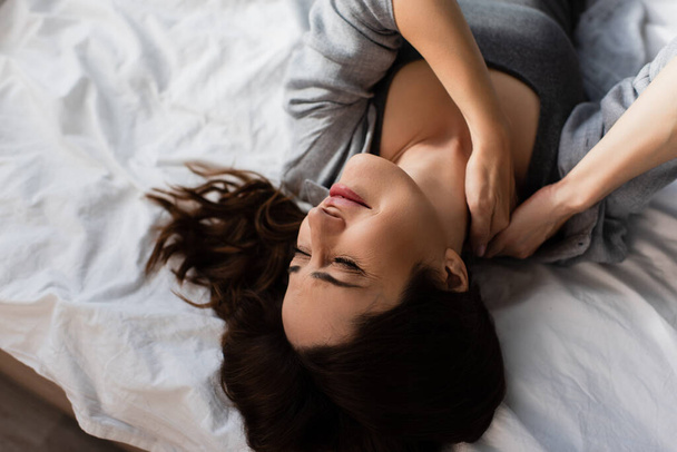 top view of displeased brunette woman suffering from neck pain in bedroom - Photo, Image