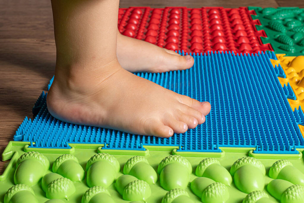 The legs of a small child on orthopedic mats. Bright surfaces for walking and forming the correct arch of the foot. Massage puzzle mat. - Foto, Bild