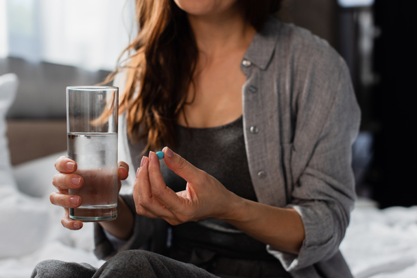 cropped view of brunette woman holding pill and glass of water at home - Φωτογραφία, εικόνα