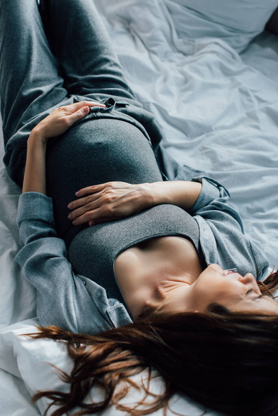 overhead view of pregnant woman suffering from pain on bed  - Foto, immagini