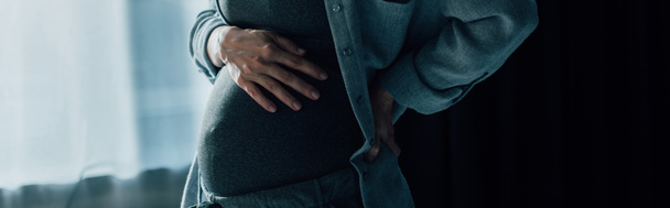панорамне поняття вагітної жінки, яка страждає від болю, торкаючись живота вдома
 - Фото, зображення