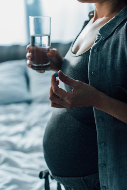 rajattu näkymä raskaana olevan naisen tilalla lasi vettä ja pilleri  - Valokuva, kuva