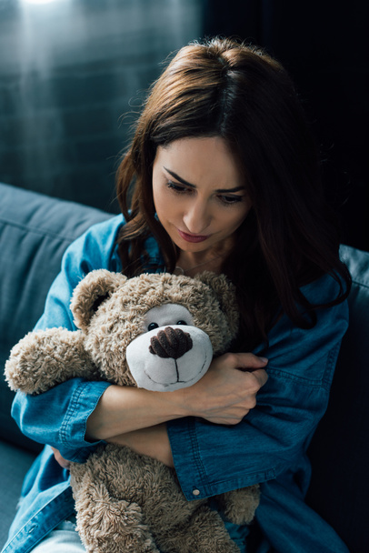 depressed brunette woman holding teddy bear and looking down  - Photo, Image