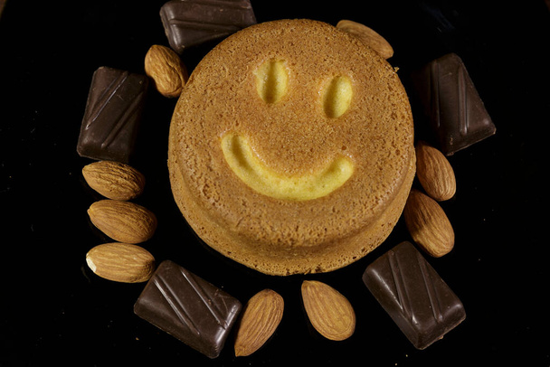 Kekse, Schokolade und Mandeln auf einem schwarzen Teller. Ansicht von oben. Dunkler Hintergrund - Foto, Bild