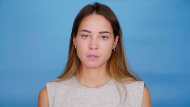 Emocionální vážná žena v šedém tričku ukazuje prostředníček na modrém pozadí - Záběry, video