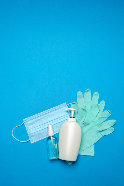 Disposable blue medical face mask, rubber latex gloves and alcohol hand sanitizer antiseptic on blue background - Foto, Bild