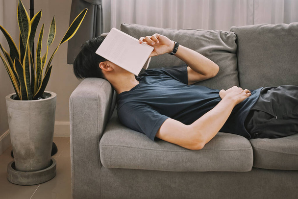 Young man nap on the sofa with book on his face at home. - Foto, Imagen