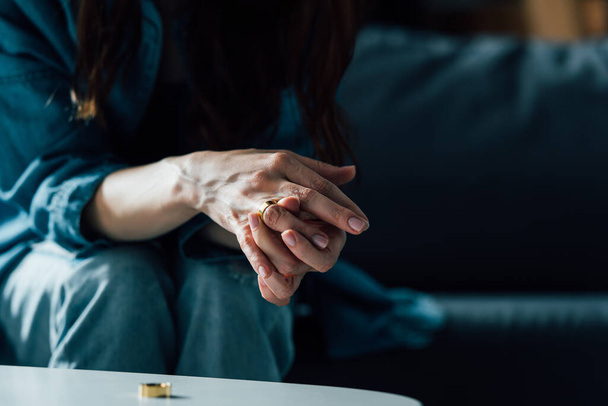 cropped view of woman sitting near coffee table and taking off golden ring, divorce concept  - Photo, Image