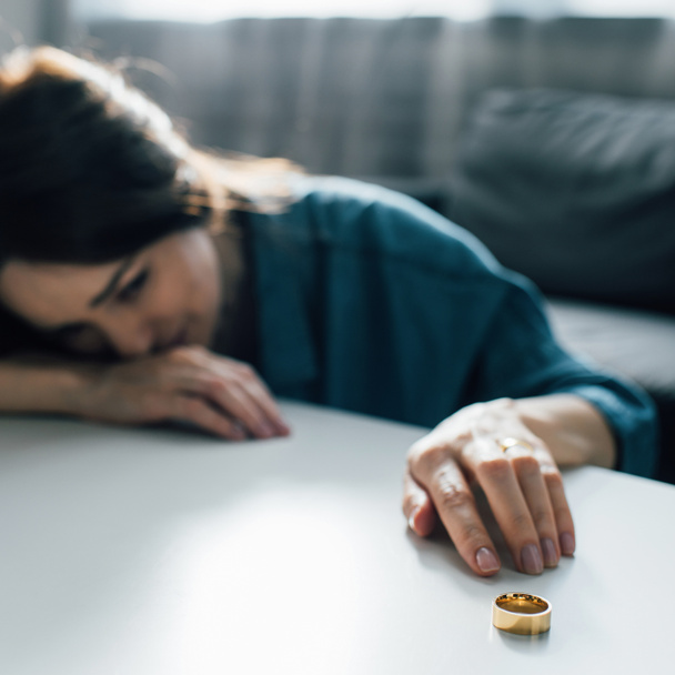 selectieve focus van trieste vrouw bereiken gouden ring op salontafel, echtscheiding concept  - Foto, afbeelding