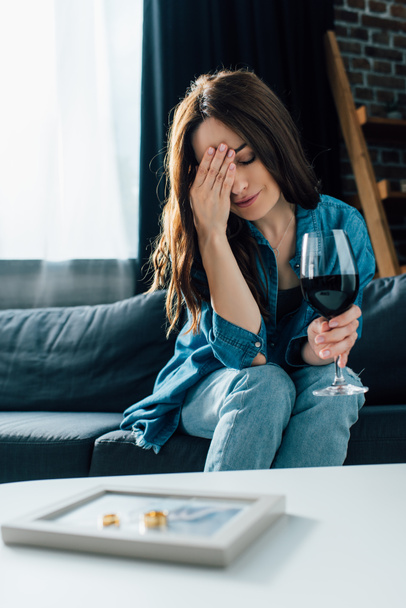 selective focus of depressed woman with glass of wine near golden rings on photo frame, divorce concept  - Photo, Image