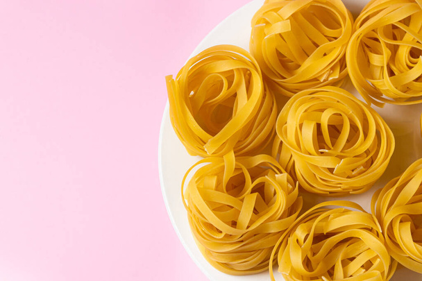 nest van pasta op een roze achtergrond. Italiaanse pasta. De pasta nesten liggen op een wit bord. Europese keuken - Foto, afbeelding