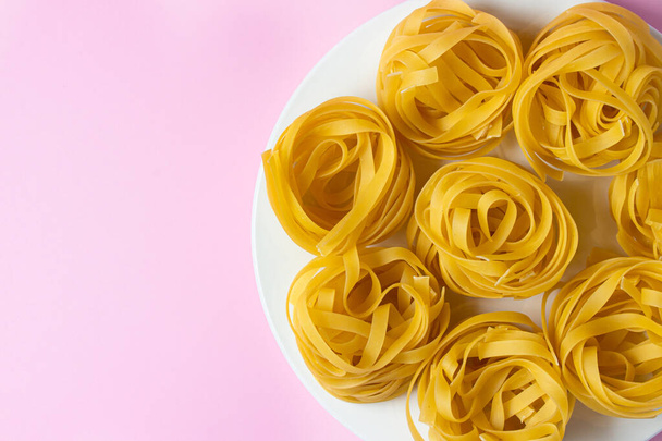 nest of pasta on a pink background. Italian pasta. The pasta nests are on a white plate. European cuisine - Foto, Bild
