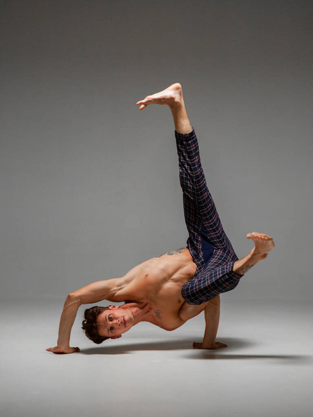Cool man dancer with naked torso dancing lower break dance isolated on gray background - 写真・画像