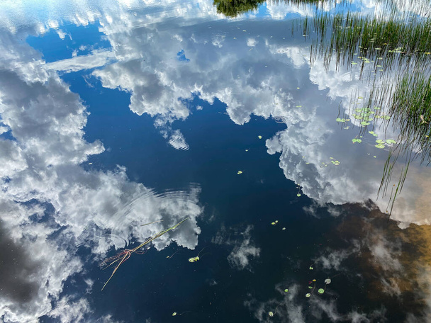 De wolken in de lucht reflecteren op een rustig meer op een mooie zomerdag. - Foto, afbeelding