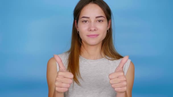 Mulher positiva bonita em camiseta cinza mostrando polegares para cima, como e sorrindo
 - Filmagem, Vídeo
